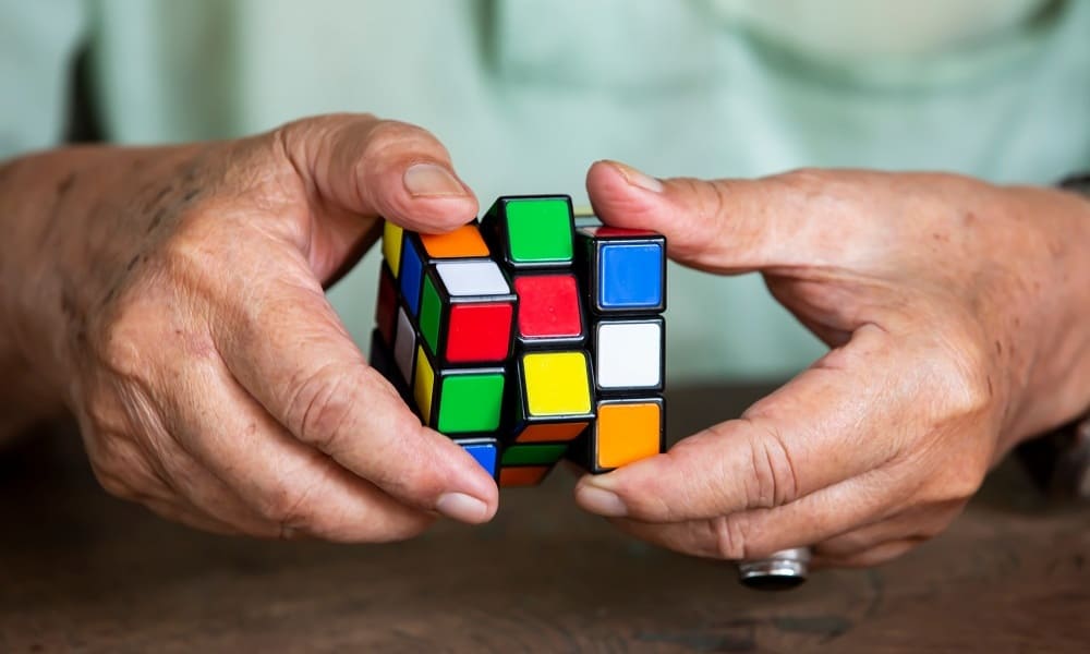 Пожилой человек собирает кубик рубика